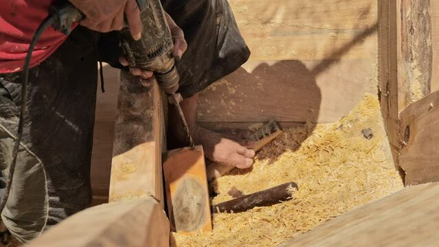 A shipbuilder is drilling a traditional wooden fishing boat on the coast of Indonesia. Close up shot without showing the face.