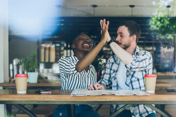 Multiracial couple high fiving after finishing planning - obrazy, fototapety, plakaty