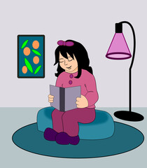 A little girl is sitting in a room reading a book, in the background is a lamp and a picture on the wall.
