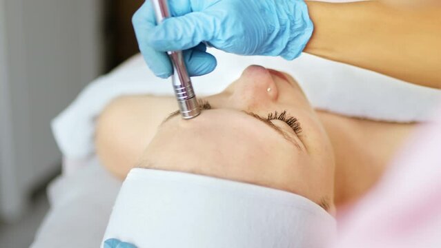 Beautician cosmetologist makes a procedure Microdermabrasion peeling of the face skin. Hardware cosmetology in clinic salon for client. Diamond face clean.