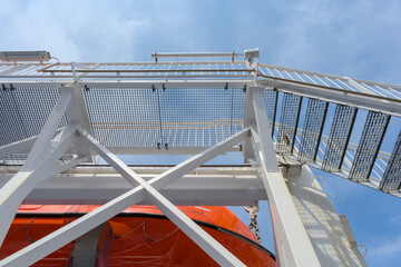 red, orange lifeboat hanging on a ferry in front of blue sky