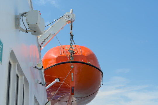 red, orange lifeboat hanging on a ferry in front of blue sky