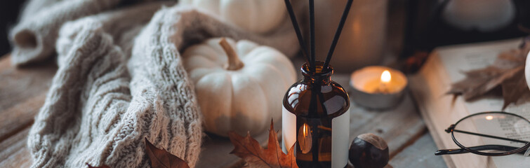 Home comfort, coziness, aromatherapy. Cozy fall interior with knitted wool warm sweater, burning candles and autumn aroma perfume diffuser. Pumpkin pie scent, maple sirup, cinnamon, anise. Banner