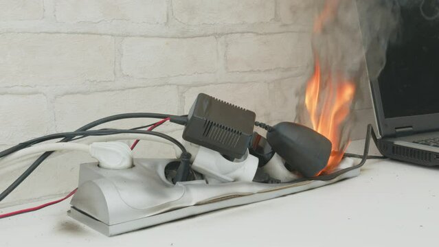 Overloaded power cube on fire on table indoors close up, voltage overload. Lot of electric plugs in sockets of power strip.