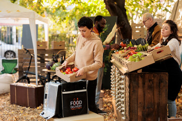 Food delivery worker putting fresh natural produce box in bag and standing at local food market....