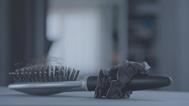 Platinum hairbrush with scrunchie on handle and knotted black hair on top. Hair broom with little tangled hairs on top spinning around on grey table