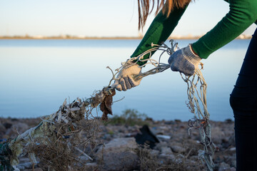 Unrecognizable female volunteer pulling a fishing net off the rocks of a polluted coastal marine...