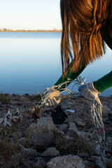 Unrecognizable volunteer pulling a fishing net off the rocks of a polluted coastal marine wetland. Vertical photo with space for text.