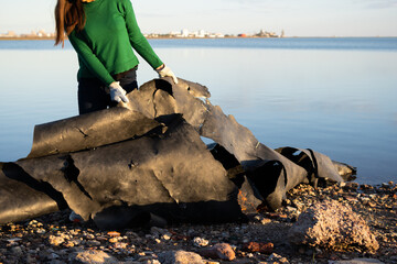 Unrecognizable volunteer removing a plastic tarp from the shore of a polluted coastal marine wetland. Photo with space for text.