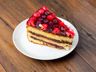 Slice of tasty multi layered cake with raspberry and blue berry in jelly on top. Portion of...