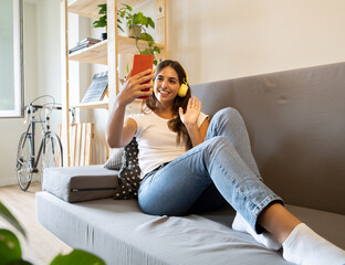 Teenage girl making a video call with smartphone in an apartment sitting on a sofa