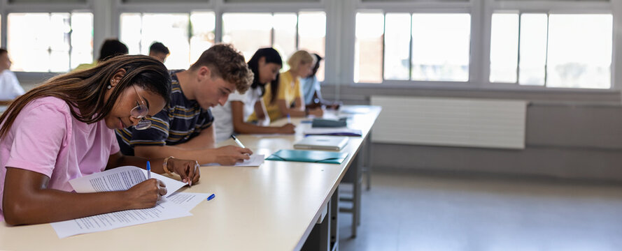 Group of diverse high school students having test exam at classroom. Education concept. Banner with copy space.