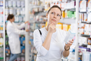 Adult woman buyer in casual clothes chooses remedy in pharmacy