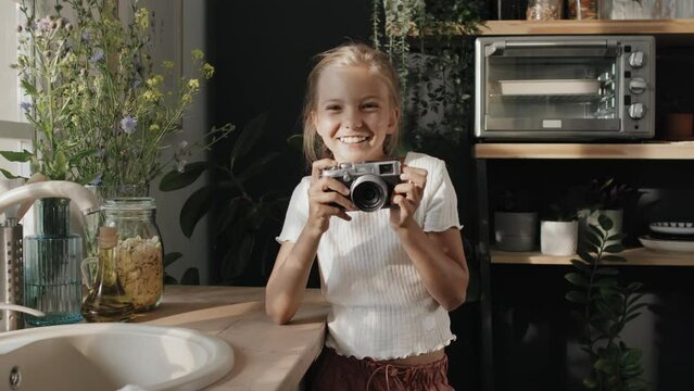 Slow motion medium portrait of modern preteen girl standing in cozy kitchen taking photo then smiling at camera