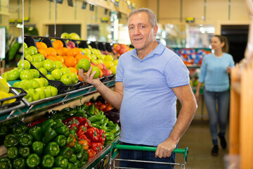 Concentrated mature male buyer pensioner choosing organic granny smith green apples in hypermarket