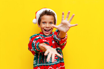 cheerful african american boy in christmas clothes throws his hands forward and shows empty palms