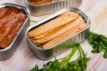 Open can of preserved natural fillet of frigate tuna on wooden table with fresh parsley ..