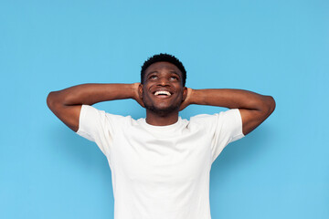 young guy african american in white t-shirt is resting and dreaming on blue isolated background