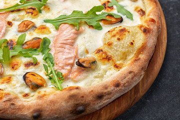Seafood pizza, marinara, di mare, with salmon, mussels and arugula, on a wooden board, against a dark background