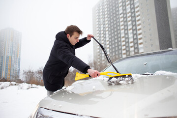 guy cleans the snow with a brush from the car, a man takes care of the car in winter