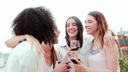 Group of happy young women friends having fun gossiping while drinking and toasting wine glasses on a rooftop party. Joyful females smiling and clinking enjoying on a social event. Ladies talking