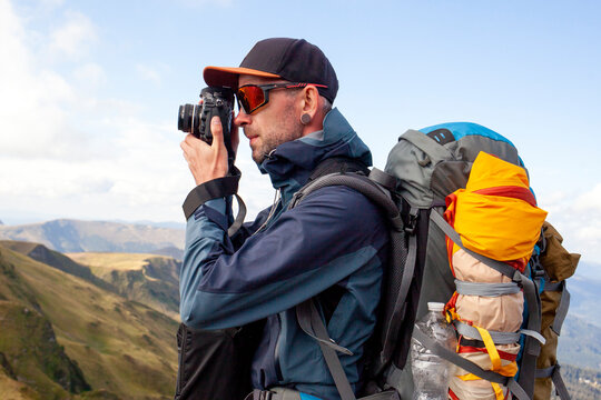 male photographer with camera takes pictures on mountain hike, guy with backpack and mountain equipment