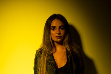 Portrait of beautiful young model with straight hair leaning on a yellow -illuminated wall.