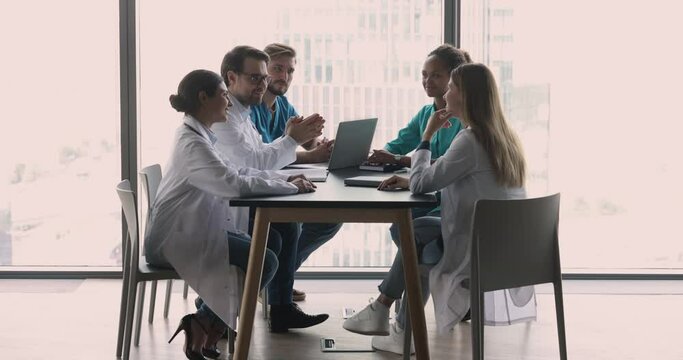 In modern clinic office group of professional medical workers attend briefing, seminar led by young and confident male head physician in white uniform. Cardiology department engaged in council event