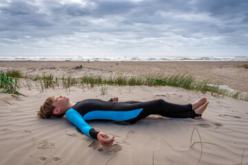 Young boy in a wet suit lying down resting on a sand dune at the beach