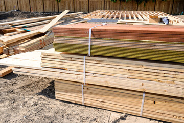 Stacks of fresh lumber delivered to a new home job site, foundation with floor joists in background
