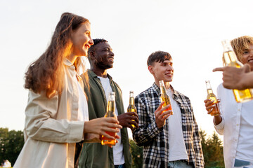 group of multiracial friends at party chatting and drinking beer outdoors, african american women and men talking