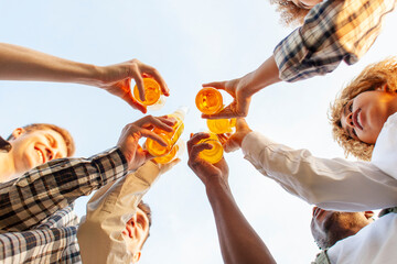 group of multiracial young people clink beer bottles outdoors, interracial students celebrating...
