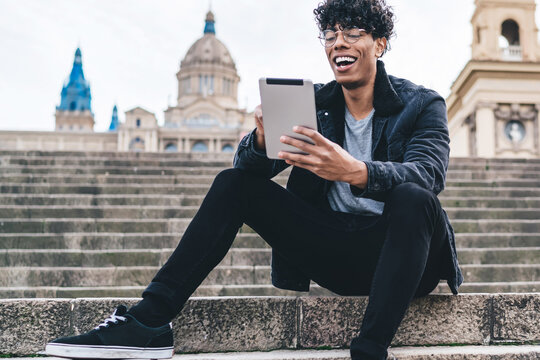 Ethnic man sitting on stairs and chatting happily via tablet