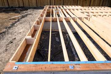 Beginnings of a new home, wood floor joists installed over concrete foundation
