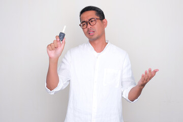 Adult Asian man looking to car key that he hold with sad expression - obrazy, fototapety, plakaty