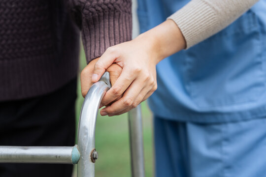 Nurse or caregiver helps elderly walk by using walker in garden