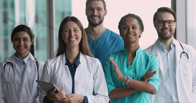 Group of confident millennial diverse doctors wear uniforms pose in clinic office. Hospital personnel team members smile look at camera standing indoors. Healthcare, medicine, professional occupation