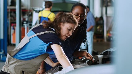 Technician in garage workspace cleaning opened up vehicle after replacing brake fluid while customer watches. Car service worker wiping automobile leftover leakage and discussing with woman