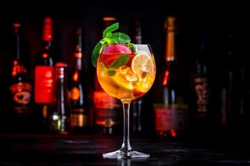 Pink sangria alcoholic cocktail drink with rose wine, peach, orange, lime and ice. Black bar counter background, steel bar tools and bottles