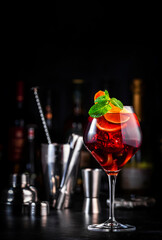 Red sangria cocktail drink with tempranillo wine, peach, plum, orange, lime and ice. Black bar counter background, steel bar tools and bottles
