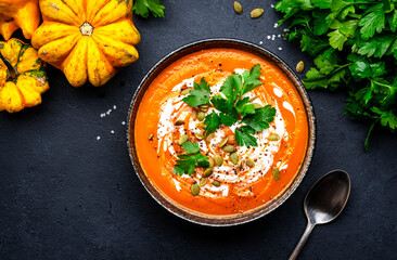 Autumn pumpkin soup puree with pumpkin seeds, cream, pepper and parsley. Winter healthy vegan slow comfort food. Soup bowl on black table background. Top view