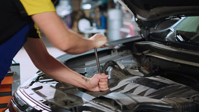Certified mechanic in car service uses wrench to tighten bolts after fixing vehicle parts. Repair shop employee utilizing professional tools to make sure automobile is properly working, close up