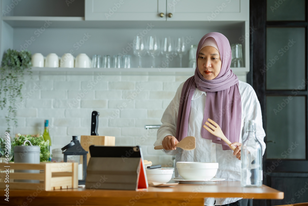 Wall mural muslim mother looking at recipe from laptop and cooking. having fun woman with hijab preparing dinner, Islamic woman Enjoying Doing Homemade, Teaching cooking online