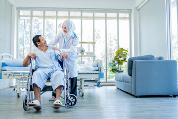 Female doctor supports patient female sitting on wheelchair. Attractive male specialist medical doctor doing physical therapy procedure for mature female for health care in hospital ward.