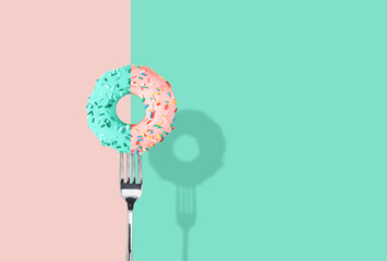 Pink and tiffany green glazed donut pricked on a fork on pink and tiffany green pastel background. Flat lay. Creative art, Contemporary style, Minimal concept of food with copy space for text.