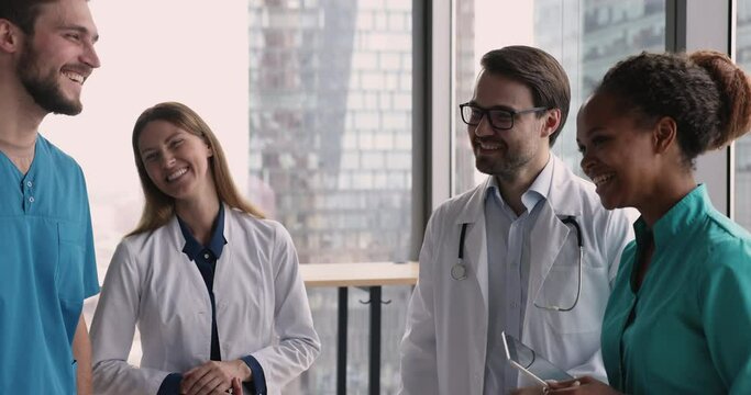 Joyful multiethnic nurses and doctors joking, laughing met in clinic hallway, ready for conference, finish briefing feel satisfied with cooperation, teamwork, friendly work relations and work results