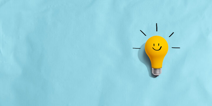 Yellow light bulb with happy face - flat lay