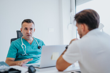 Fototapeta premium Experienced doctor and young patient reviewing x-ray results in hospital office. Diagnosis and treatment discussion for health issues.