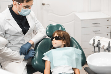 Professional young male dentist working with little girl in clinic.