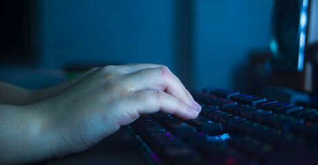 Close-up of female hands working on a computer keyboard at night - obrazy, fototapety, plakaty